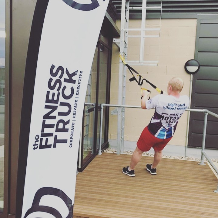 man using suspension trainers next to The Fitness Truck sign